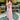 Woman in a pink traditional outfit standing outdoors with greenery and tables in the background
